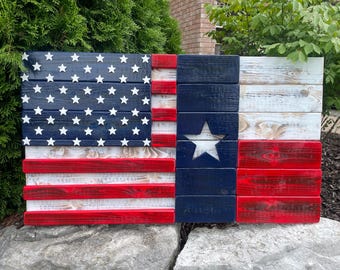 Op de afbeelding: Een Amerikaanse vlag en een Texaanse vlag van hout, gecombineerd tot één stuk. De vlaggen zijn geschilderd in rood, wit en blauw met een verweerde look. De Texaanse vlag heeft een witte ster in het midden.