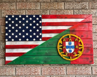 Op de afbeelding: Een houten bord met de Amerikaanse vlag aan de linkerkant en de Portugese vlag aan de rechterkant. De vlaggen zijn geschilderd op houten planken en komen samen in een diagonale hoek.