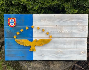 Op de afbeelding: Houten wandkunst met een vlagontwerp met blauwe, witte en gele accenten. De vlag bevat een wapen, sterren en een gouden adelaar. Het hout heeft een verweerde, rustieke uitstraling.