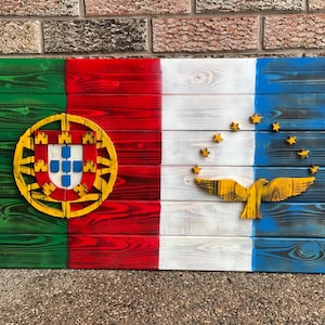 Peut inclure: Une enseigne en bois peinte avec les drapeaux du Portugal et du Timor oriental. Le drapeau portugais présente un fond vert et rouge avec un blason jaune. Le drapeau timorais présente un fond blanc avec un oiseau jaune et des étoiles.