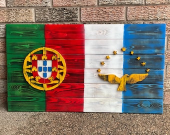 Op de afbeelding: Een houten bord met de vlaggen van Portugal en Oost-Timor erop geschilderd. De Portugese vlag heeft een groene en rode achtergrond met een geel wapenschild. De Oost-Timorese vlag heeft een witte achtergrond met een gele vogel en sterren.