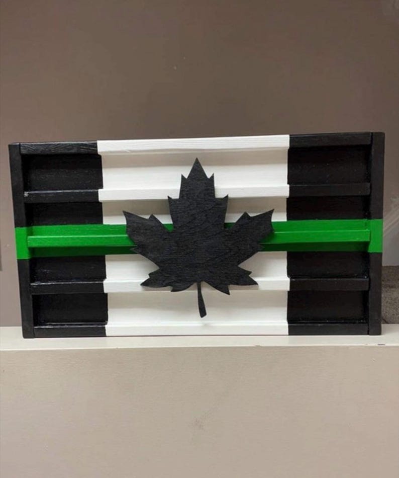 May include: A wooden sign with a black and white striped background and a green stripe across the middle. A black maple leaf is centered on the sign.
