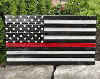 Op de afbeelding: Een Amerikaanse vlag van hout met een rode streep in het midden, geschilderd in zwart en wit. De vlag is gemaakt van afzonderlijke houten planken.