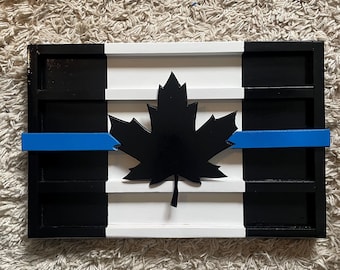 Op de afbeelding: Een houten Canadese vlag met een blauwe lijn in het midden, die steun voor rechtshandhaving symboliseert. De vlag is zwart, wit en blauw geverfd en heeft een zwart esdoornblad in het midden.