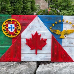 May include: A wooden sign featuring four flags painted on it. The flags are the flags of Portugal, Canada, the United States, and the flag of the Azores. The sign is crafted from reclaimed wood and has a rustic appearance.