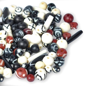May include: A selection of mixed beads in different shapes and sizes. The beads are mainly black, white, and red, featuring decorative designs. Some are cylindrical, others round or oval. These beads are suitable for jewellery making or crafting projects.