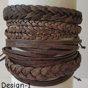 Op de afbeelding: Een verzameling bruine leren armbanden, waaronder gevlochten en platte ontwerpen. De armbanden zijn op elkaar gestapeld en tonen verschillende texturen en stijlen. De afbeelding bevat de tekst "Design-1" linksonder.