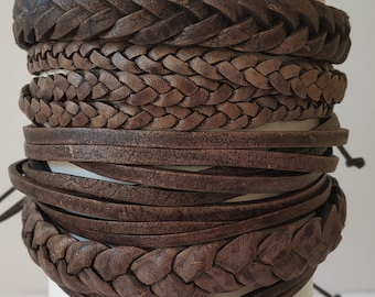 May include: A collection of brown leather bracelets, including braided and flat designs. The bracelets are stacked, showcasing various textures and styles. The image includes the text "Design-1" at the bottom left.