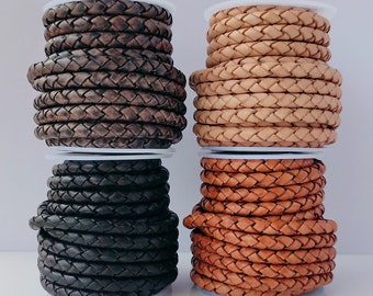 Puede incluir: Cuatro carretes de cordón de cuero trenzado en diferentes colores: marrón, tostado, negro y marrón oscuro. Los cordones están enrollados alrededor de carretes blancos.