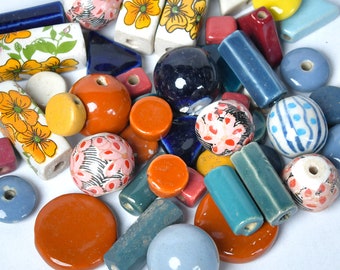 May include: A collection of colourful ceramic beads and tiles in various shapes and sizes. The beads are decorated with floral patterns, stripes, and polka dots. The tiles are in shades of blue, green, and orange.