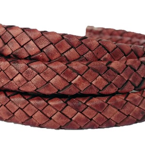 May include: A close-up of a brown leather cord with a braided design. The cord is woven in a square pattern and is approximately 1/2 inch wide.