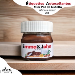 Peut inclure: Un petit pot de Nutella en verre avec un couvercle blanc, étiqueté "Emma & John" et la date du 25.05.23. L'étiquette comprend des illustrations de toasts au Nutella, un verre de lait, des noisettes et une fleur jaune. Le pot contient 25g de Nutella.