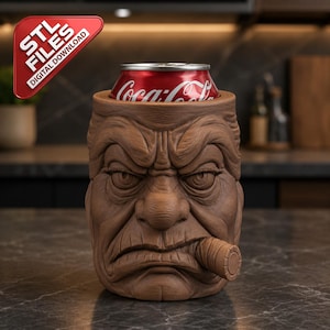 Può includere: Un refrigeratore per lattine cilindrico marrone con un volto umano scolpito e imbronciato, rughe profonde, sopracciglia aggrottate e un sigaro in bocca. Una lattina rossa di Coca-Cola è inserita sopra. Un cartello rosso indica STL FILES DIGITAL DOWNLOAD.