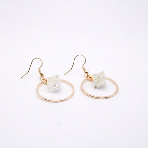 May include: A pair of gold-colored hoop earrings with a clear, square-shaped crystal accent. The earrings have a simple, elegant design, perfect for everyday wear. The hooks are gold-colored.