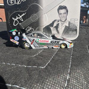 May include: A silver and black Castrol GTX X 1:64 scale Funny Car model with the text "Castrol GTX" and "John Force". The packaging features Elvis Presley and a guitar. Limited edition adult collectible.