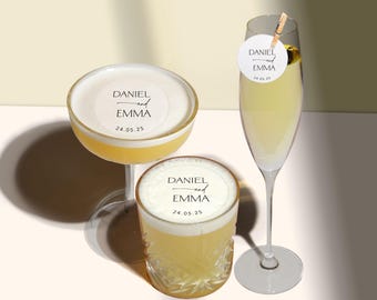 Puede incluir: Dos vasos de cóctel de vidrio transparente con una pegatina blanca en el borde que dice "Daniel y Emma 24.05.25". Un vaso es un vaso de copa y el otro es un vaso de rocas.
