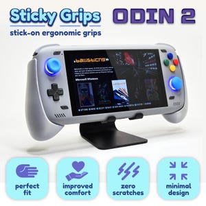 Könnte beinhalten: Eine hellgraue Handheld-Spielkonsole mit blauen Analogsticks und bunten Aktionstasten, mit dem Text Sticky Grips ODIN 2. Das Gerät steht auf einem schwarzen Ständer, darunter vier hellblaue Symbole mit den Beschriftungen perfect fit, improved comfort, zero scratches, minimal design.