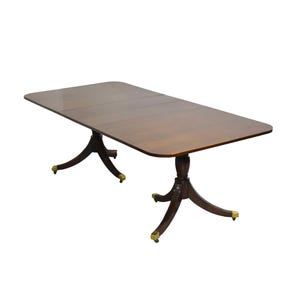 May include: A rectangular wooden dining table with a dark brown finish. The table has a pedestal base with three curved legs and brass-colored accents. The table measures approximately 72 inches long.