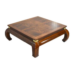 May include: Square coffee table with a dark wood grain top and a rich, glossy finish. The table has curved legs and brass accents, creating a sophisticated, vintage aesthetic. A stylish piece of furniture for a living room.