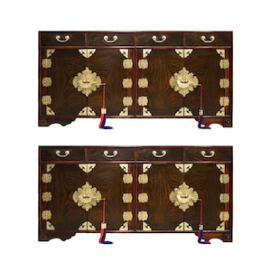 May include: Two dark wood cabinets with ornate brass hardware and floral accents. Each cabinet has multiple drawers and doors, with decorative tassels hanging from the doors. The cabinets are likely used for storage.
