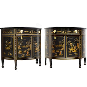 May include: Two black, semi-circular cabinets with gold painted Asian-inspired landscape scenes. Each cabinet has a drawer with a gold pull and a gold tassel. The cabinets have four black legs.