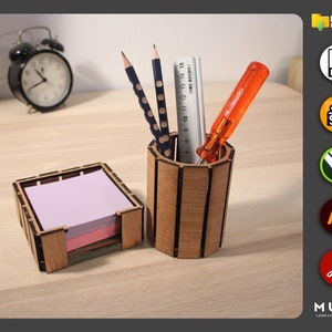 May include: A wooden desk organizer set with a pencil holder and a note pad holder. The pencil holder has a cylindrical shape and is made of wood with vertical grooves. The note pad holder is a square box with a slot for holding note pads. The set is made of natural wood and has a rustic look.