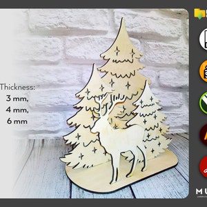 May include: Laser cut wooden Christmas decoration featuring a deer standing in front of two stylized Christmas trees. The trees have stars and are decorated with a simple line design. The deer has antlers and a simple design. The decoration is available in 3 mm, 4 mm, and 6 mm thicknesses.
