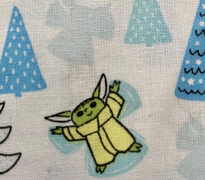 May include: A green and yellow cartoon character with large ears and a robe, making a snow angel on a white background with blue and white Christmas trees.