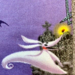 May include: A purple fabric with a white and gray image of Jack Skellington from The Nightmare Before Christmas. Jack is holding a glowing orb and is standing in front of a tombstone.