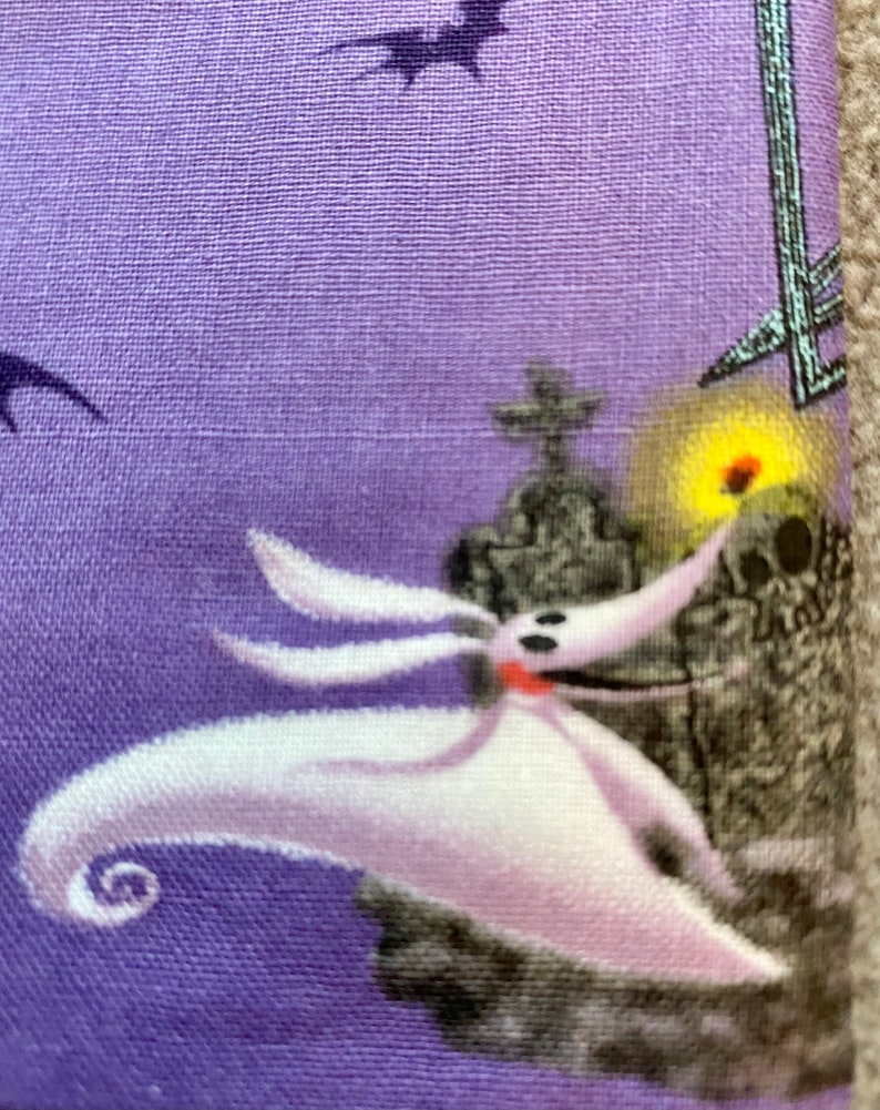May include: A purple fabric with a white and gray image of Jack Skellington from The Nightmare Before Christmas. Jack is holding a glowing orb and is standing in front of a tombstone.