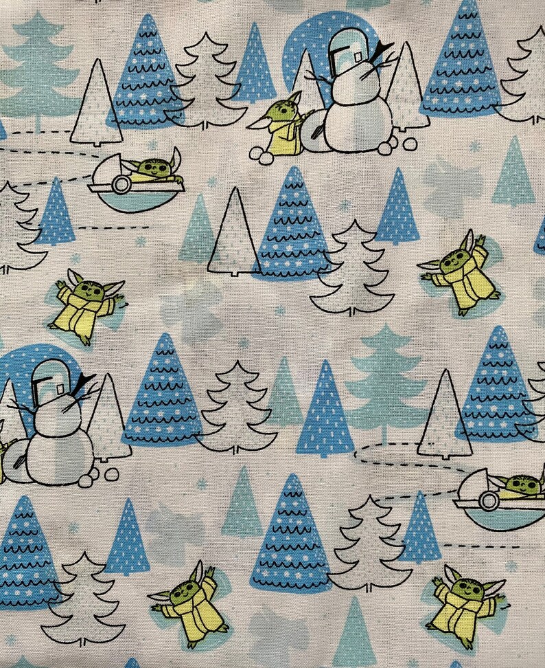 May include: A white fabric with a repeating pattern of blue and green Christmas trees, snowmen, and small green characters. The characters are wearing yellow robes and have large ears.