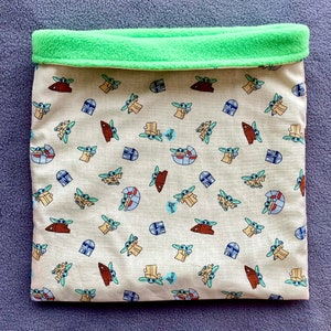May include: A beige fabric pet bed with a green fleece lining. The fabric features a repeating pattern of small green characters with a blue helmet and a brown creature.