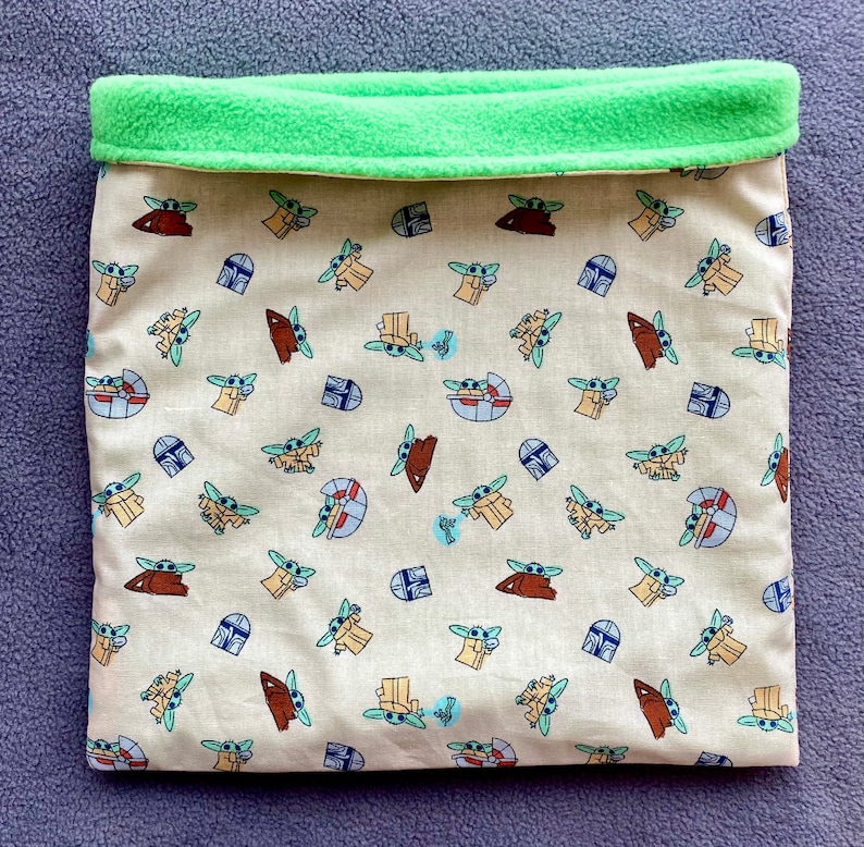 May include: A beige fabric pet bed with a green fleece lining. The fabric features a repeating pattern of small green characters with a blue helmet and a brown creature.