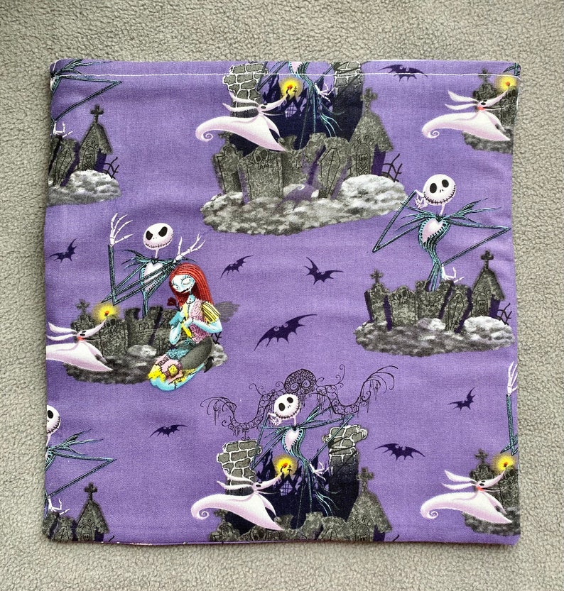 May include: Purple fabric with a repeating pattern of Jack Skellington and Sally from The Nightmare Before Christmas. The characters are depicted in a graveyard setting with bats and tombstones.