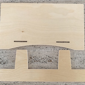 Side-angle view of a natural birch plywood 18-inch book display stand holding an open, multi-page catalog on a wooden table against a white background.