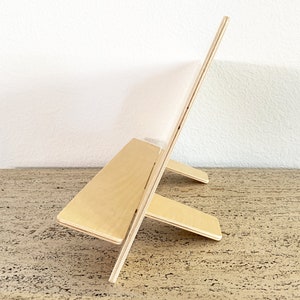 Profile view of a wooden countertop display stand showing the slim depth, angled lip, and back support legs on a neutral surface.