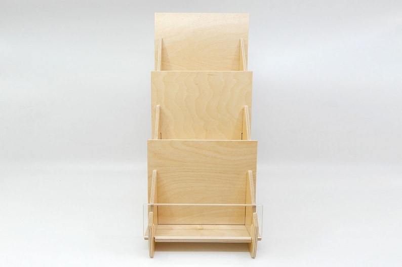 A three-tiered wooden display stand with a clear acrylic shelf on the bottom. The stand is made of natural wood and has a simple, modern design.