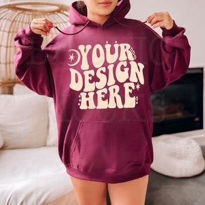 May include: A maroon hoodie with a white pocket and the text "YOUR DESIGN HERE" in a retro font with stars and a crescent moon.