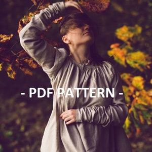 May include: A woman wearing a long, light grey dress with long sleeves. The dress has a gathered neckline and a simple design. The woman is standing in a woodland setting with autumn foliage in the background. The text "PDF PATTERN" is superimposed on the image.