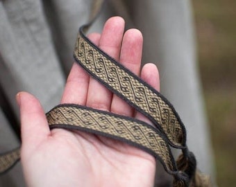 Puede incluir: Dos correas tejidas marrones y negras con borlas. Las correas tienen un patrón geométrico.