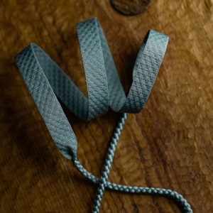 Puede incluir: Primer plano de un cord&oacute;n trenzado azul verdoso con una superficie texturizada. El cord&oacute;n est&aacute; anudado y retorcido, creando un dise&ntilde;o decorativo.