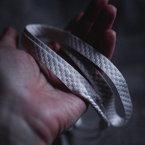 Puede incluir: Un cintur&oacute;n de tela blanco texturizado se sostiene en una mano. El cintur&oacute;n est&aacute; doblado por la mitad y los extremos se superponen.