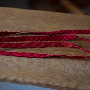 Puede incluir: Tres cordones de tela roja con un patr&oacute;n de diamante. Los cordones est&aacute;n sobre una superficie de madera.