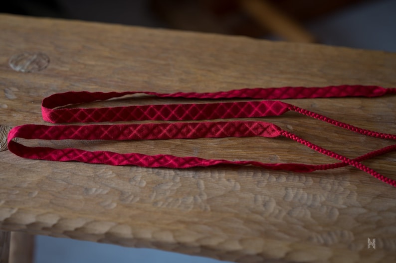 Puede incluir: Tres cordones de tela roja con un patr&oacute;n de diamante. Los cordones est&aacute;n sobre una superficie de madera.