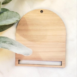 May include: A natural wood half-circle sign with a slot at the bottom for hanging. The sign has a hole at the top for hanging.