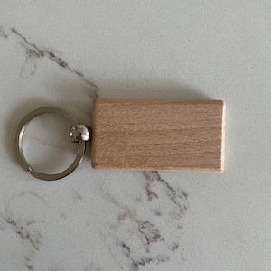 May include: A wooden keychain with a blank rectangular tag attached to a silver metal ring.