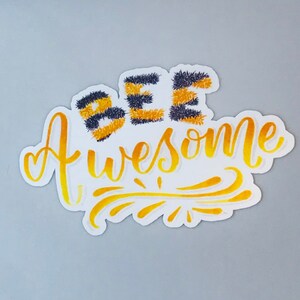 May include: A white sticker with the text "Bee Awesome" in yellow and black. The word "Bee" is made up of three stylised bees with black and yellow stripes.