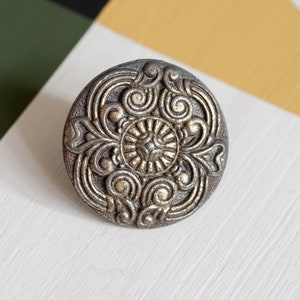 May include: A round, ornate, metal button with a gold finish and a detailed floral design.