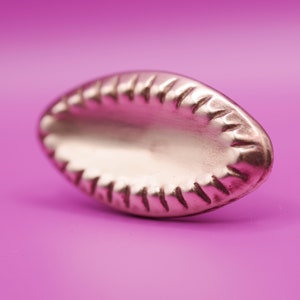 May include: A silver-coloured, oval-shaped, decorative metal piece with a textured, scalloped edge.