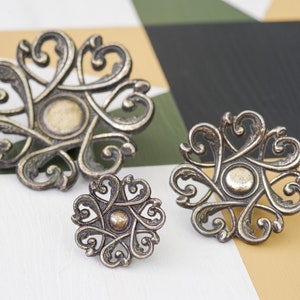 May include: Three ornate metal drawer pulls with a floral design. The pulls are in shades of silver and gold.